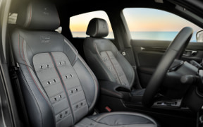 Dark gray leather front seats with sporty bolsters and square stitching, steering wheel and dashboard visible in a car cabin at sunset outside the window.
