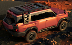 Orange off-road SUV with roof rack sits on rocky desert terrain at sunset.