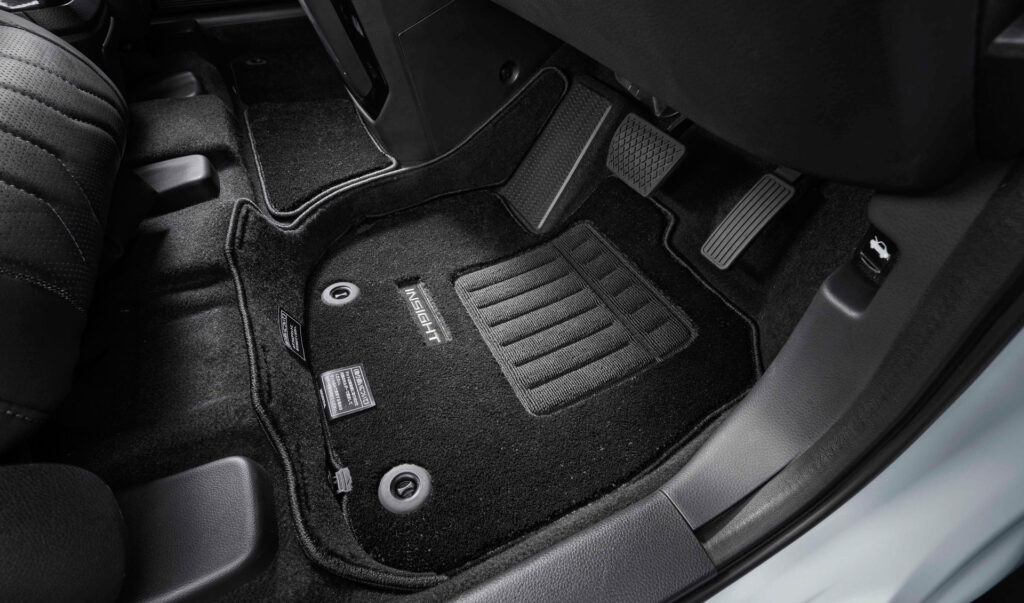 Driver's side car floor with a black textured floor mat and visible pedals (gas and brake).