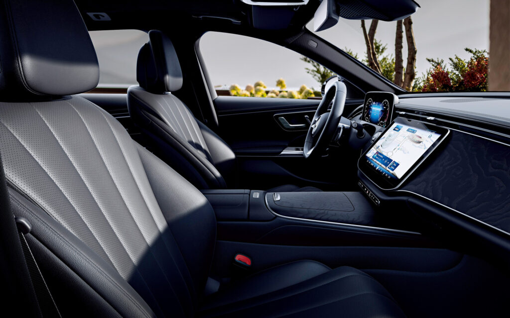 Interior of a luxury car with two large touchscreen displays and gray perforated leather seats in the front row.