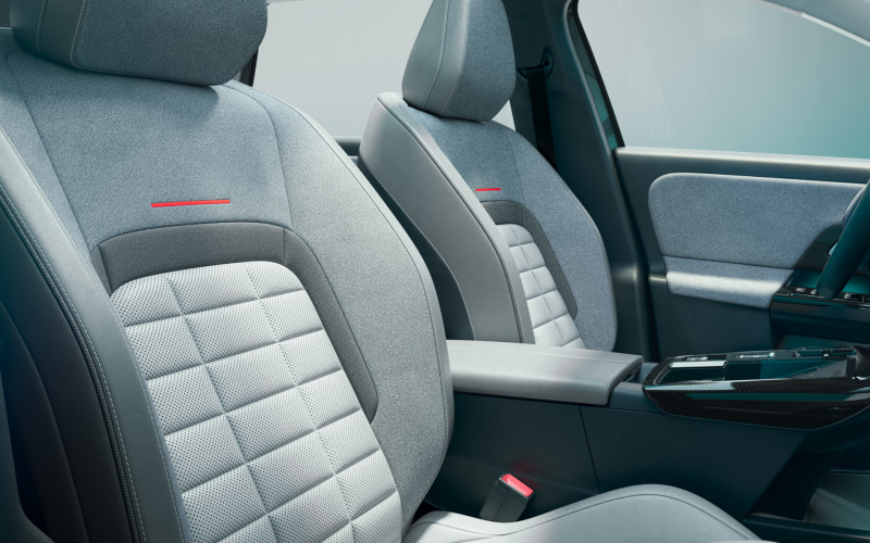 Interior of a modern car showing two front seats with light gray perforated upholstery, red accent lines, and a center console between them.
