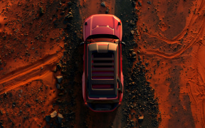 Top-down view of a red SUV driving on orange-red dirt terrain.