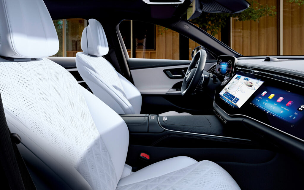 Luxury car interior with white quilted leather seats and a digital dashboard surface behind the steering wheel in view, conveying premium comfort and tech.