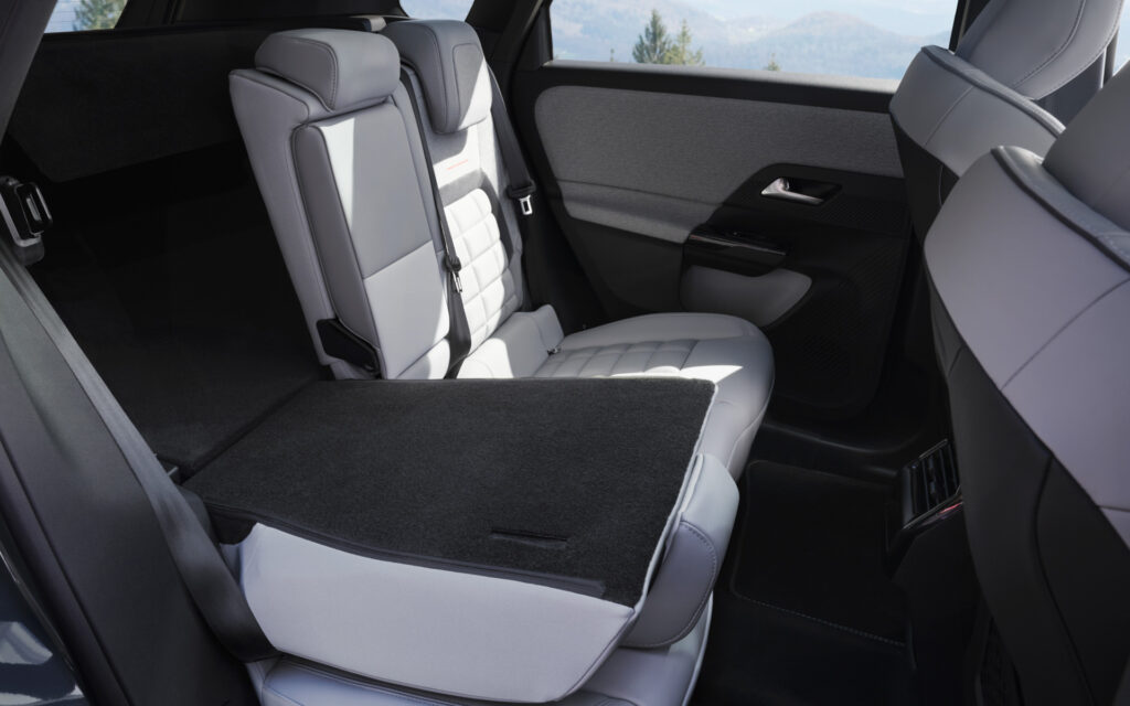 Interior of a car with a folded rear seat creating a flat loading floor, light gray upholstery.