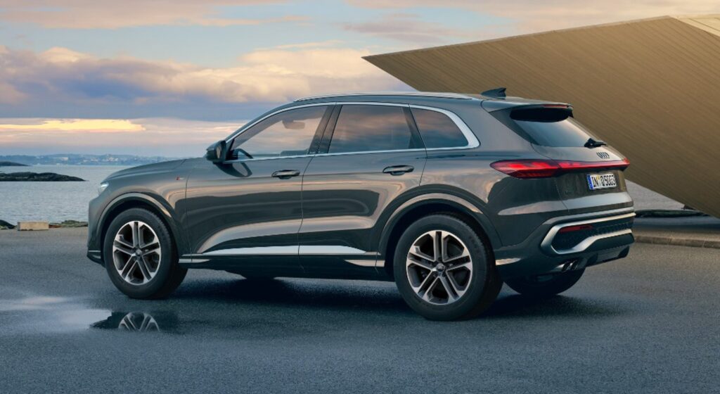 Gray SUV parked on a wet promenade by the water with a large wooden ramp in the background at sunset.