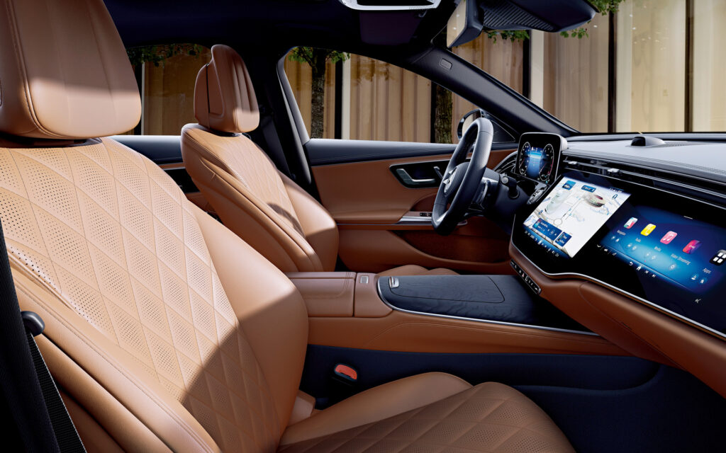 Luxurious car interior with tan quilted leather seats, digital dash, and wide touchscreen infotainment center.