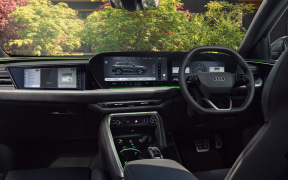 Interior of a modern car cockpit with a digital instrument cluster, central touchscreen, and steering wheel (Audi) visible; trees outside the windshield.