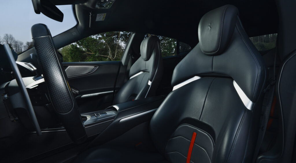 Interior of a luxury sports car with black perforated leather bucket seats and orange seatbelt accents.