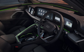 Dark Audi concept car interior with digital cockpit, large screens, and green ambient lighting along the dash and doors.