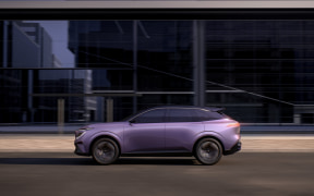 Purple crossover SUV driving along a city street with glass office buildings in the background.