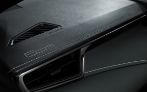 Close-up of a dark car dashboard with stitched leather and a small air vent grille visible in the foreground.