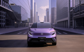Front view of a purple car on a city street with tall glass buildings in the background.