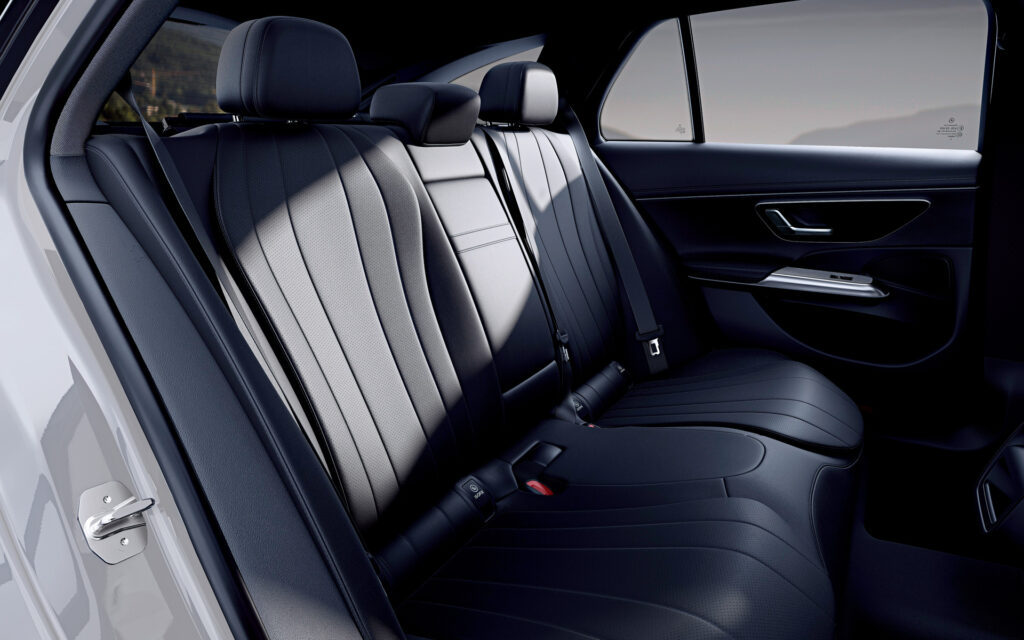 Rear seating area with three black leather seats, headrests, and visible seat belts in a car interior