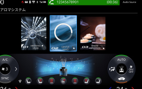 Car infotainment screen showing aroma system option, three media thumbnails, and climate control dials below.