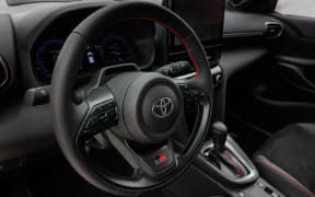 Steering wheel with Toyota emblem, red stitching, and dashboard visible inside a car interior.