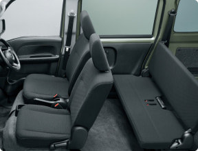 Interior of a compact car showing two front seats and a folded rear bench, revealing dark fabric upholstery and small cargo space.