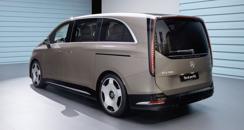 Rear-three-quarter view of a brown Mercedes-Benz VLE 300 minivan in a studio with blue walls in the background, showcasing its design.