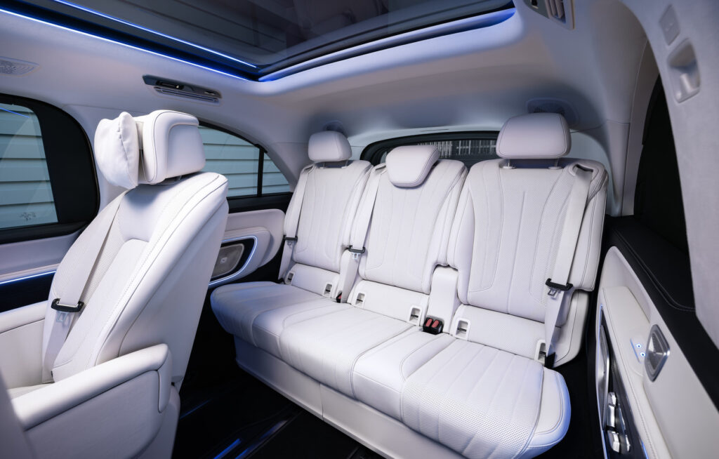 White leather SUV interior with three-row seating and blue ambient lighting from a panoramic sunroof behind the driver seat.