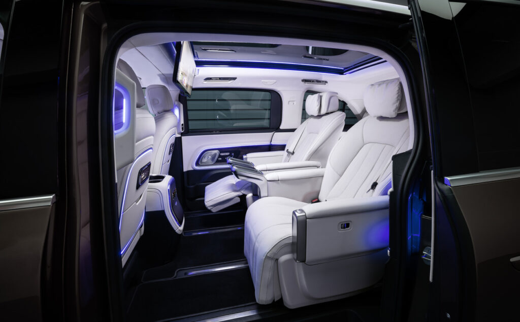 Inside a luxury vehicle: white leather rear captain seats, blue ambient lighting, and open door showing a spacious cabin area in a premium SUV