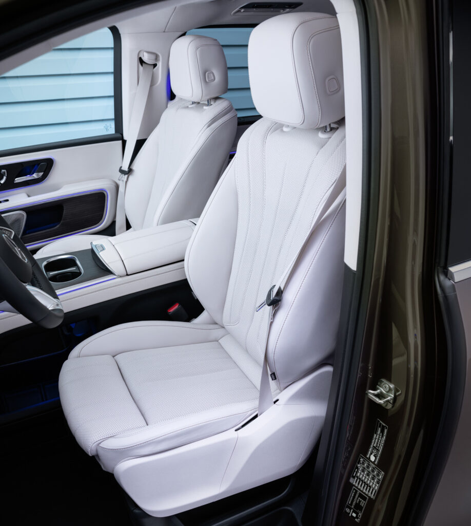 Luxurious light gray perforated leather front seats in a Mercedes‑Benz, with a center console and blue ambient lighting outside view