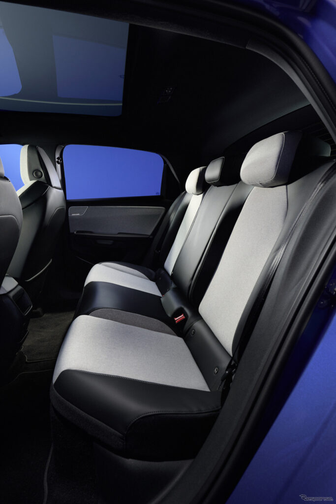 Rear passenger seats in a modern car with light gray and black upholstery and a panoramic sunroof above.