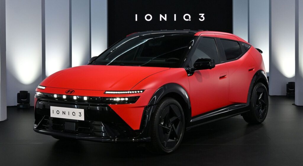 Front three-quarter view of a red Hyundai Ioniq 3 concept car on display in a showroom, with 'IONIQ 3' signage behind it.