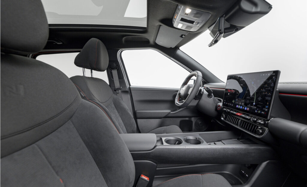 Dark, modern car interior with front seats, center console, and a large touchscreen dashboard visible from the passenger area, sunroof open above.