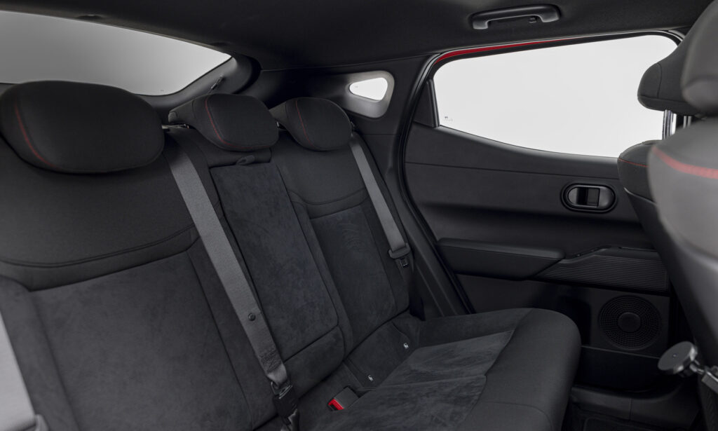 Rear car seat view: black fabric seats with red-stitched headrests and three seat belts in a modern hatchback.