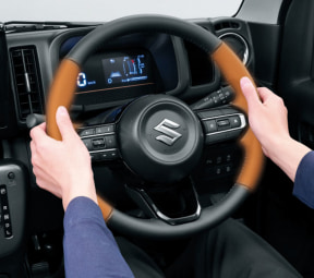 Close-up of hands gripping a brown steering wheel inside a Suzuki car, with the digital instrument cluster visible in the background.