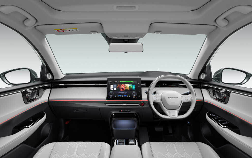Right-hand drive car interior with steering wheel on the right, large central touchscreen, and gray seats.